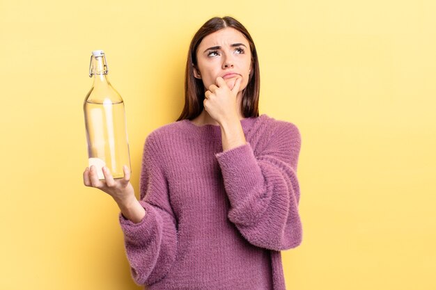 Giovane donna ispanica che pensa, si sente dubbiosa e confusa. concetto di bottiglia d'acqua