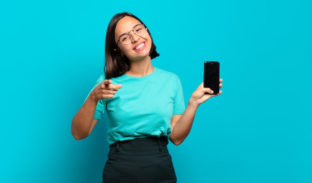 Giovane donna ispanica che punta alla telecamera con un sorriso soddisfatto, fiducioso, amichevole, scegliendo te