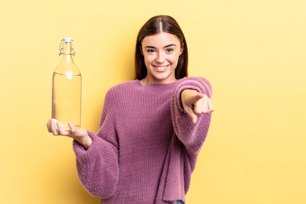 Giovane donna ispanica che punta alla telecamera scegliendo te. concetto di bottiglia d'acqua