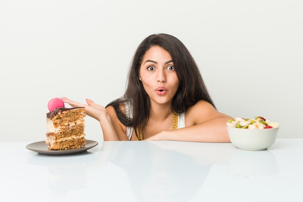 Giovane donna ispanica che sceglie fra la torta o la frutta colpita