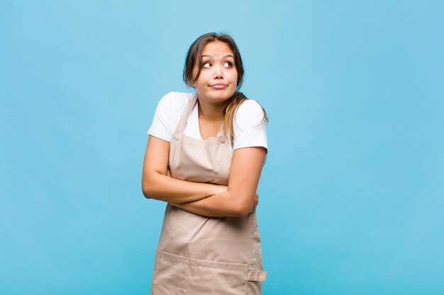 Giovane donna ispanica che scrolla le spalle, sentendosi confusa e incerta, dubbiosa con le braccia incrociate e lo sguardo perplesso