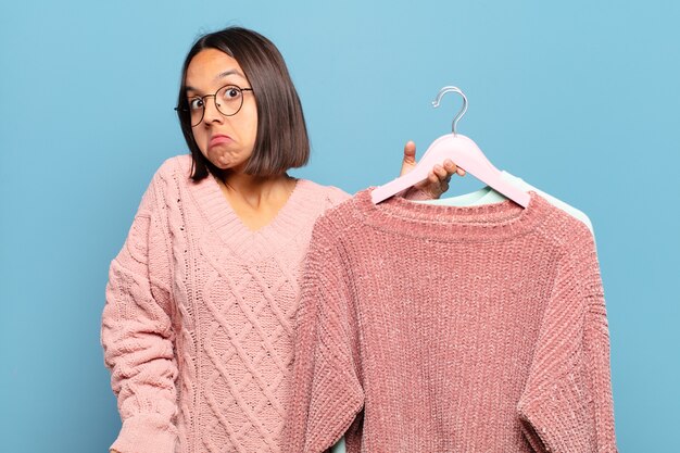 Giovane donna ispanica che scrolla le spalle, si sente confusa e incerta, dubitando con le braccia incrociate e lo sguardo perplesso