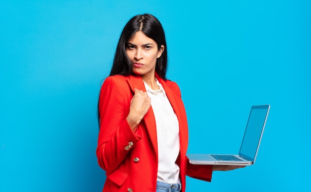 Giovane donna ispanica che sembra arrogante, di successo, positiva e orgogliosa, che indica se stessa. concetto di laptop