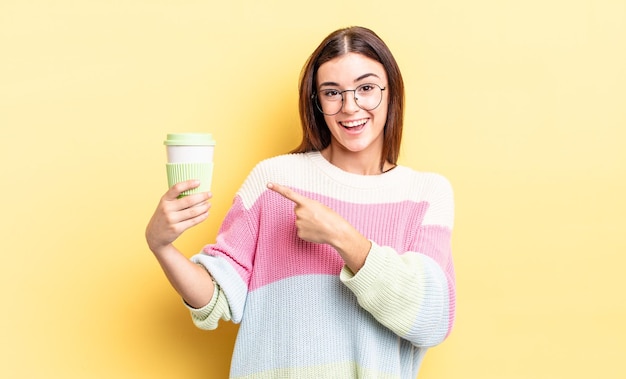 Giovane donna ispanica che sembra eccitata e sorpresa che indica il concetto di caffè da asporto laterale