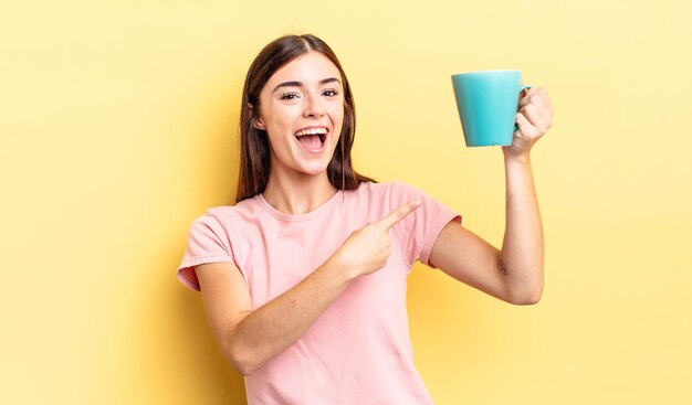 Giovane donna ispanica che sembra eccitata e sorpresa indicando il lato. concetto di tazza di caffè