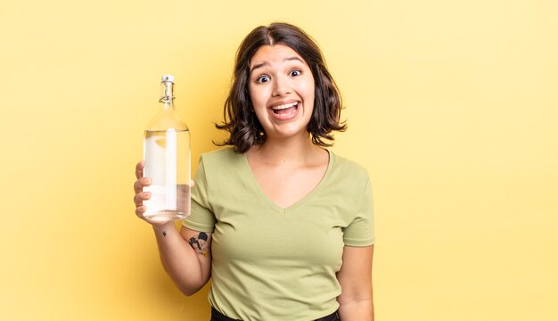 Giovane donna ispanica che sembra felice e piacevolmente sorpresa. concetto di bottiglia d'acqua