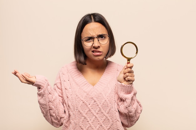 Giovane donna ispanica che sembra perplessa, confusa e stressata, chiedendosi tra diverse opzioni, sentendosi incerta