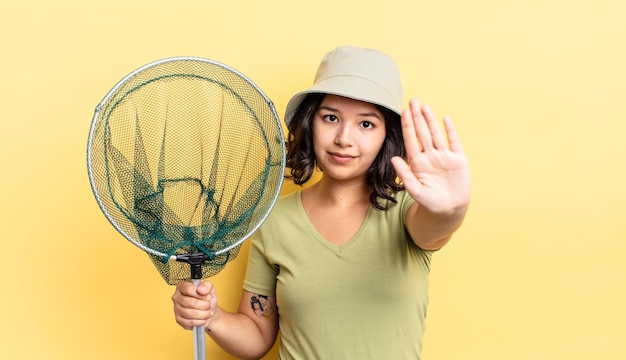 Giovane donna ispanica che sembra seria mostrando palmo aperto che fa gesto di arresto. concetto di rete da pescatore
