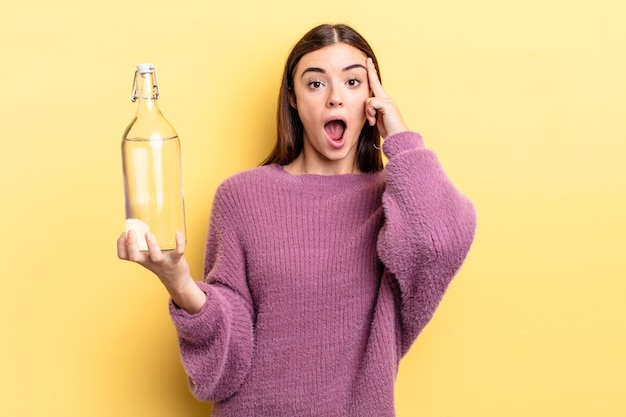 Giovane donna ispanica che sembra sorpresa, realizzando un nuovo pensiero, idea o concetto. concetto di bottiglia d'acqua