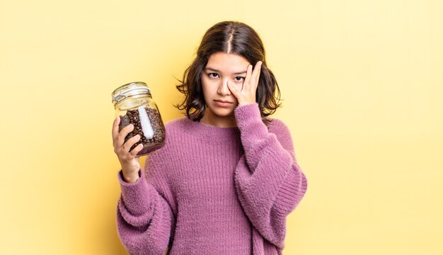 Giovane donna ispanica che si sente annoiata, frustrata e assonnata dopo una noiosa. concetto di chicchi di caffè