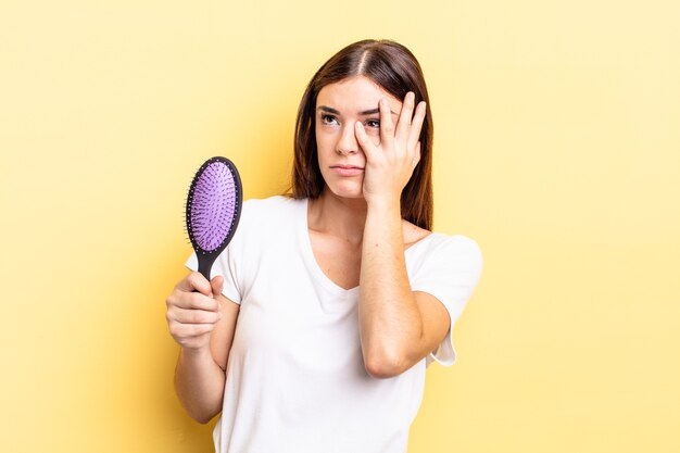 Giovane donna ispanica che si sente annoiata, frustrata e assonnata dopo una noiosa. concetto di spazzola per capelli