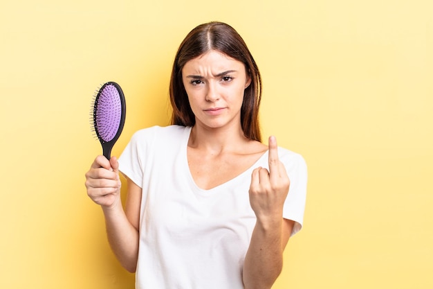 Giovane donna ispanica che si sente arrabbiata, infastidita, ribelle e aggressiva concetto di spazzola per capelli