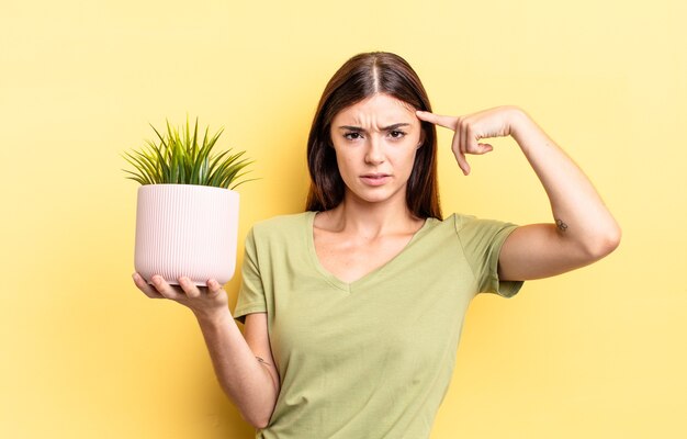 giovane donna ispanica che si sente confusa e perplessa, mostrando che sei pazzo. concetto di vaso per piante