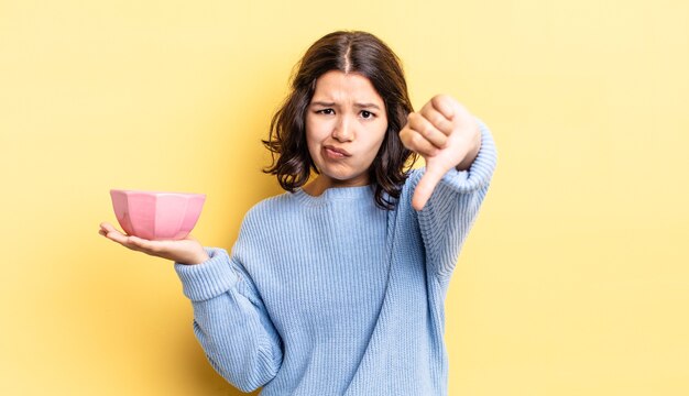 Giovane donna ispanica che si sente croce, che mostra i pollici verso il basso. concetto di ciotola vuota