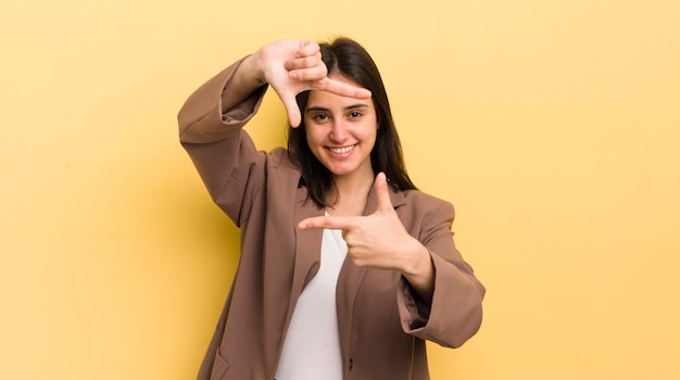 Giovane donna ispanica che si sente felice, amichevole e positiva, sorridente e fa un ritratto o una cornice per foto con le mani