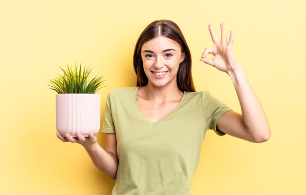 Giovane donna ispanica che si sente felice, mostrando approvazione con un gesto ok. concetto di vaso per piante