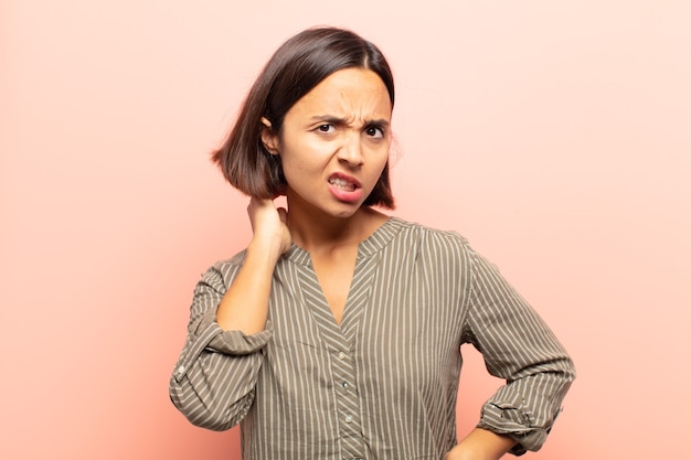 Giovane donna ispanica che si sente stressata, frustrata e stanca, strofinando il collo doloroso, con uno sguardo preoccupato e turbato