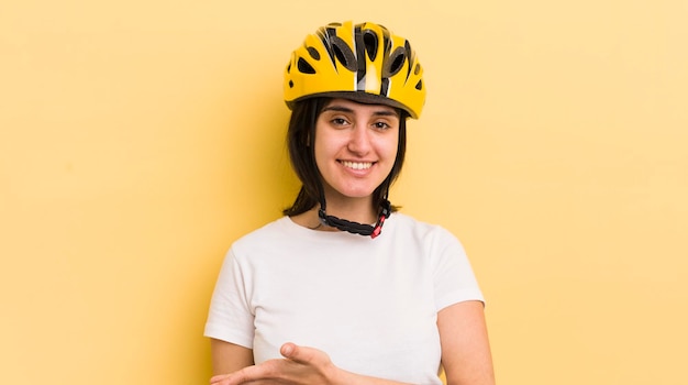 Giovane donna ispanica che sorride allegramente sentendosi felice e mostrando un concetto di casco da bici di concetto