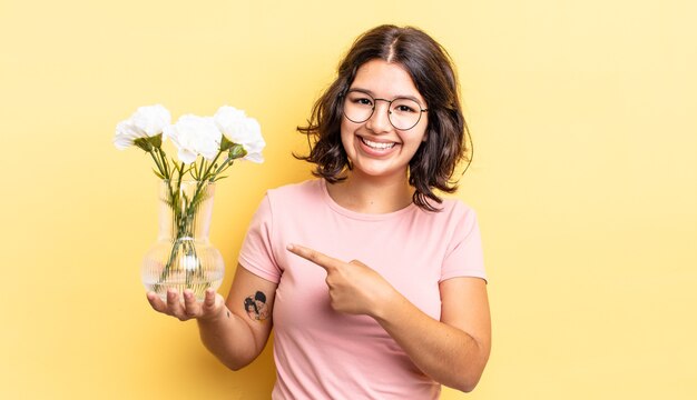 Giovane donna ispanica che sorride allegramente, si sente felice e indica il lato. concetto di vaso di fiori