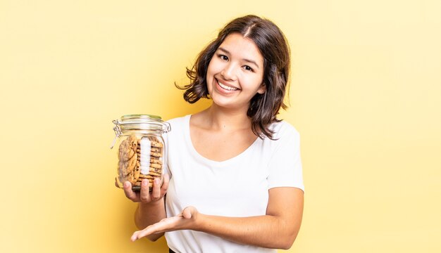 Giovane donna ispanica che sorride allegramente, si sente felice e mostra un concetto. concetto di bottiglia di biscotti