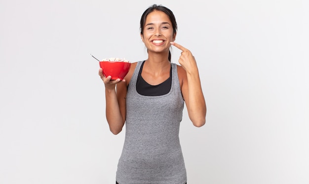 Giovane donna ispanica che sorride con sicurezza indicando il proprio ampio sorriso. dieta fitness e concetto di colazione