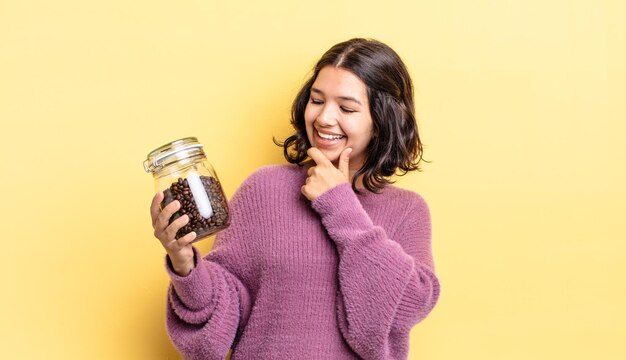 Giovane donna ispanica che sorride con un'espressione felice e sicura con la mano sul mento. concetto di chicchi di caffè