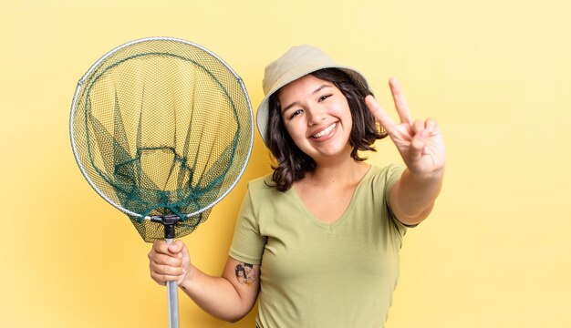 Giovane donna ispanica che sorride e che sembra felice, gesticolando vittoria o pace. concetto di rete da pescatore