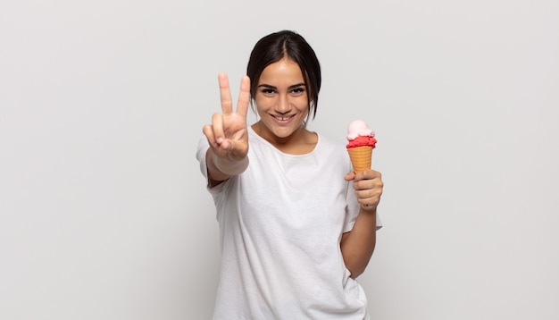 Giovane donna ispanica che sorride e che sembra felice, spensierata e positiva, gesticolando vittoria o pace con una mano