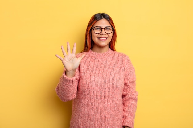 Giovane donna ispanica che sorride e sembra amichevole, mostrando il numero cinque o quinto con la mano in avanti, il conto alla rovescia