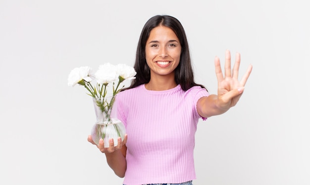 Giovane donna ispanica che sorride e sembra amichevole, mostrando il numero quattro che tiene in mano dei fiori decorativi