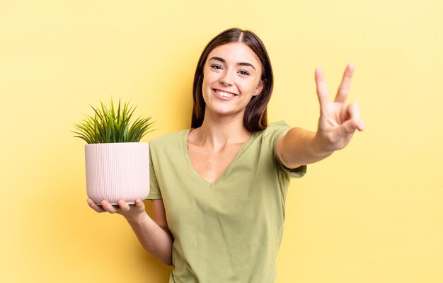 Giovane donna ispanica che sorride e sembra felice, gesticolando vittoria o pace. concetto di vaso per piante