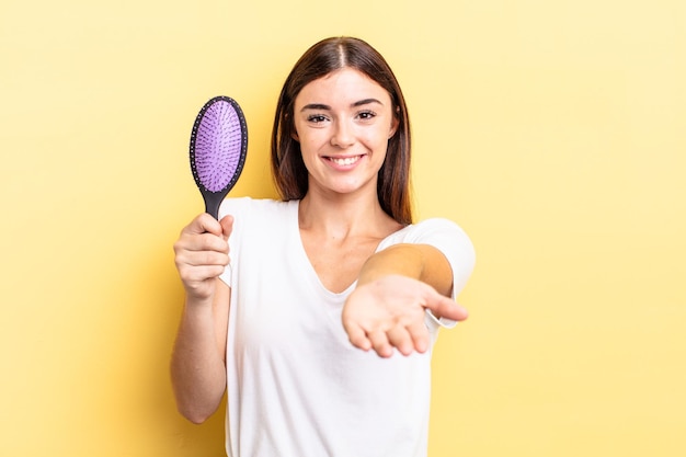 Giovane donna ispanica che sorride felicemente con amichevole e offrendo e mostrando un concetto. concetto di spazzola per capelli