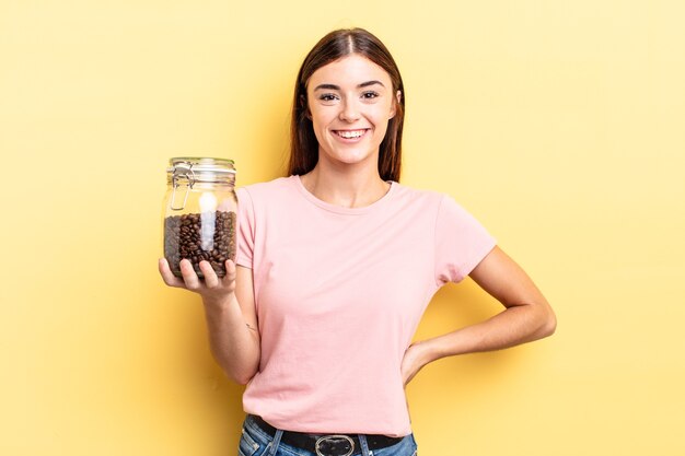 Giovane donna ispanica che sorride felicemente con una mano sull'anca e sicura di sé. concetto di chicchi di caffè