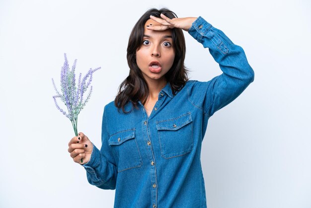 Giovane donna ispanica che tiene lavanda isolata su sfondo bianco facendo un gesto a sorpresa mentre guarda di lato