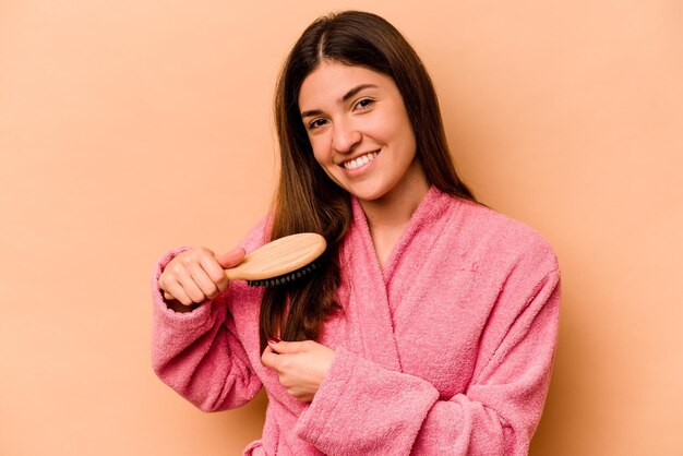 Giovane donna ispanica che tiene spazzola per capelli isolata su sfondo beige