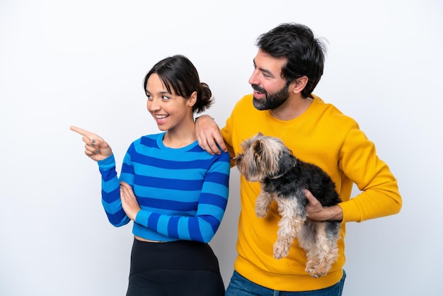 Giovane donna ispanica che tiene un cane isolato su sfondo bianco che indica il lato per presentare un prodotto