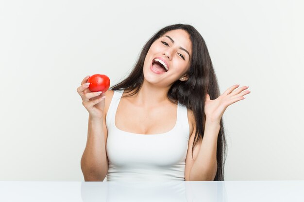 Giovane donna ispanica che tiene un pomodoro che celebra una vittoria o un successo