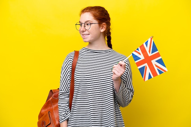 Giovane donna ispanica che tiene una bandiera del Regno Unito isolata su sfondo giallo guardando il lato