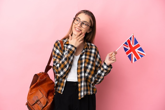 Giovane donna ispanica che tiene una bandiera del Regno Unito isolata sul rosa che osserva in su mentre sorride