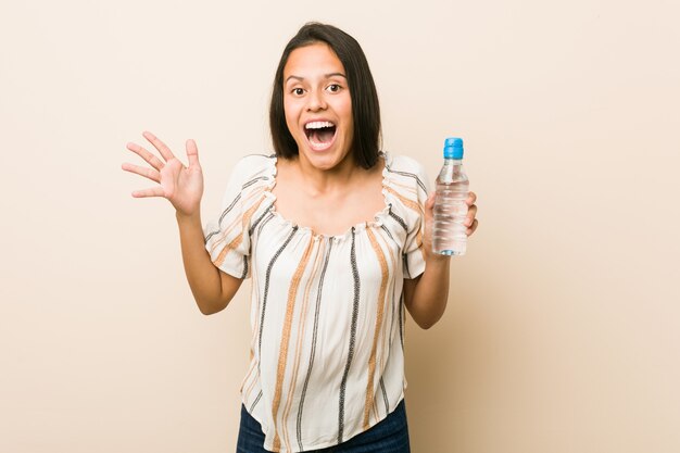 Giovane donna ispanica che tiene una bottiglia di acqua per celebrare una vittoria o un successo