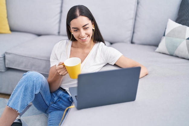 Giovane donna ispanica che utilizza il computer portatile che beve caffè a casa