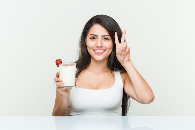 Giovane donna ispanica con un frullato giovane donna ispanica con un avocadoast che mostra il segno di vittoria e che sorride ampiamente. <Mixto>