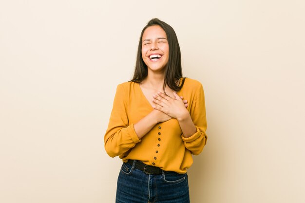 Giovane donna ispanica contro una parete beige che ride tenendo le mani sul cuore, concetto di felicità.