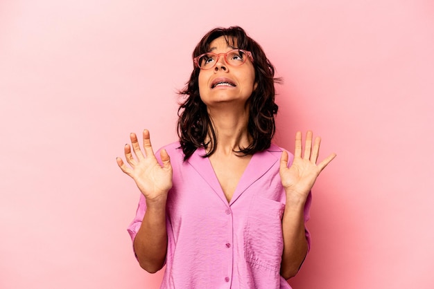 Giovane donna ispanica isolata su sfondo rosa che grida al cielo che osserva in su frustrata