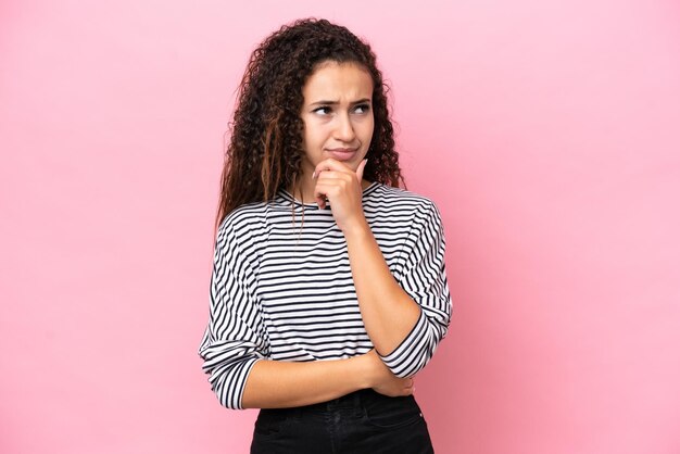 Giovane donna ispanica isolata su uno sfondo rosa che pensa a un'idea mentre guarda in alto