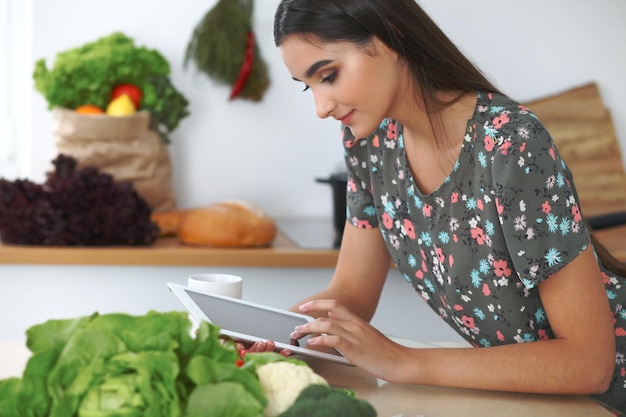 Giovane donna ispanica o studente che cucina in cucina Ragazza che utilizza tablet per fare acquisti online o trovare una nuova ricetta