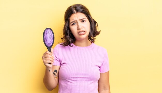 Giovane donna ispanica sentirsi perplessa e confusa. concetto di spazzola per capelli