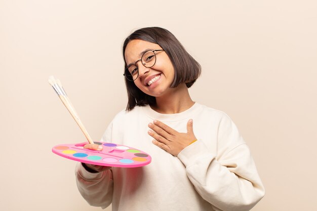 Giovane donna ispanica sentirsi romantica, felice e innamorata, sorridendo allegramente e tenendosi per mano vicino al cuore