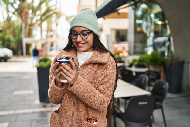 Giovane donna ispanica sorridente caffè bevente fiducioso in strada