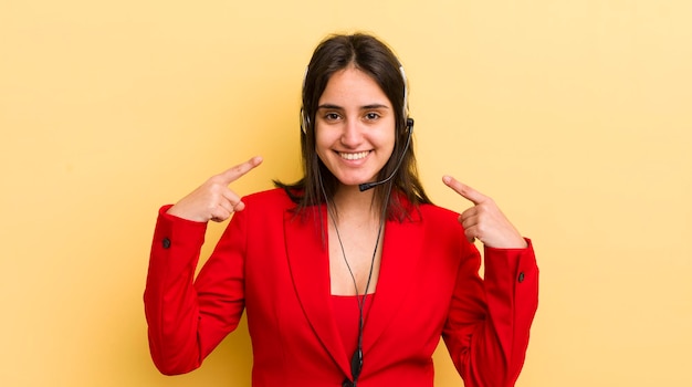 Giovane donna ispanica sorridente che punta con sicurezza al proprio concetto di telemarketing ampio sorriso